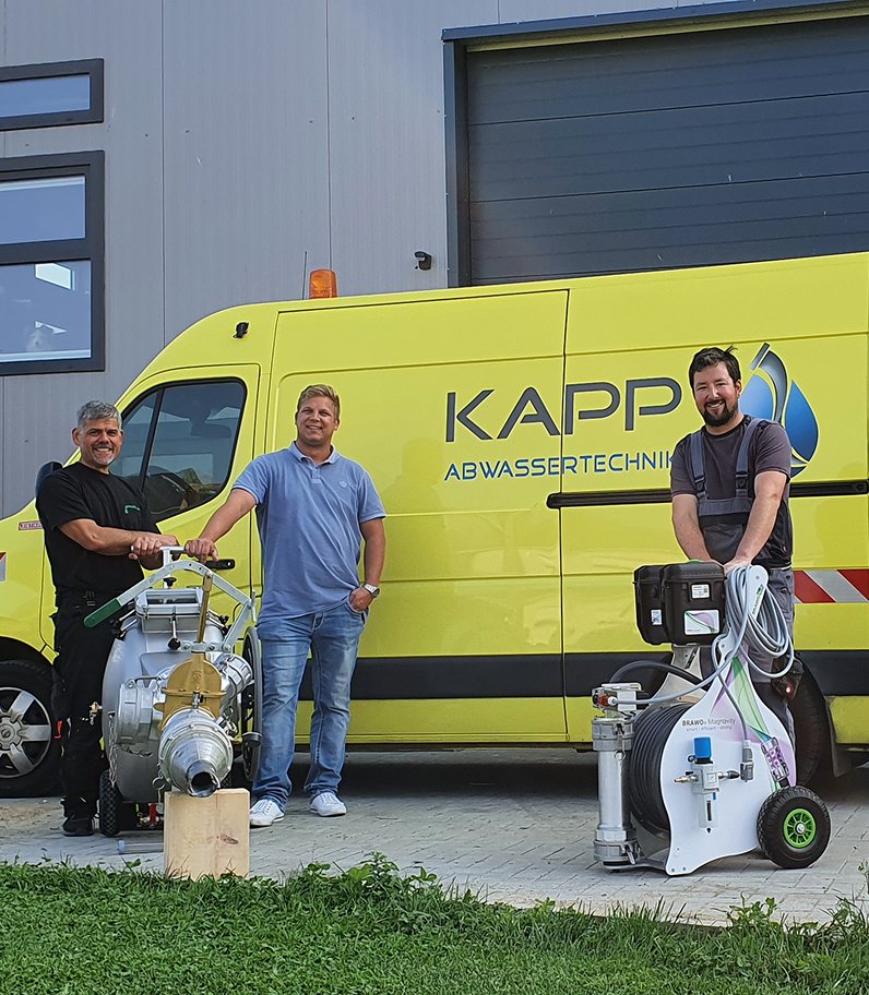 Mitarbeiter von Abwassertechnik Kapp mit Arbeitsgeräten für die Rohrsanierung stehen vor einem gelben Firmenfahrzeug.